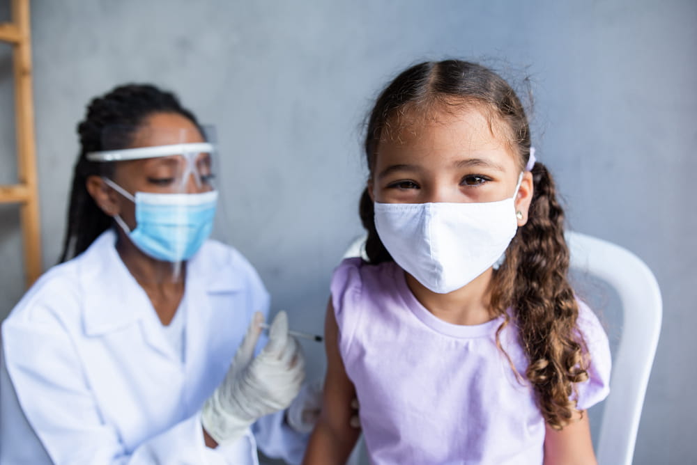 A kid smiling as a health care worker administers a shot