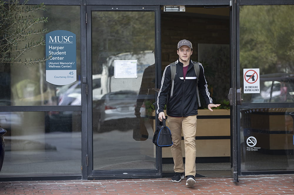 A man wearing a hat exiting a building through a glass door