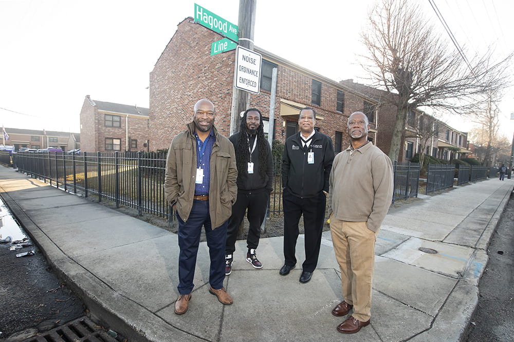 group photo of four men standing on the corner in front of public housing