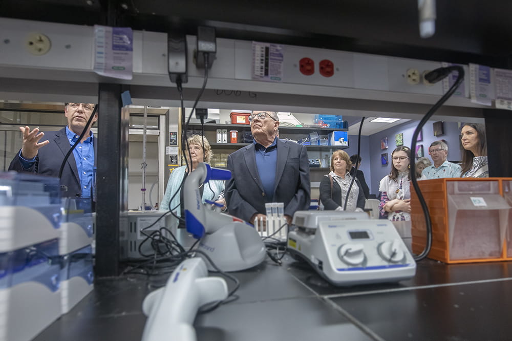 As seen through shelving, people look around a lab