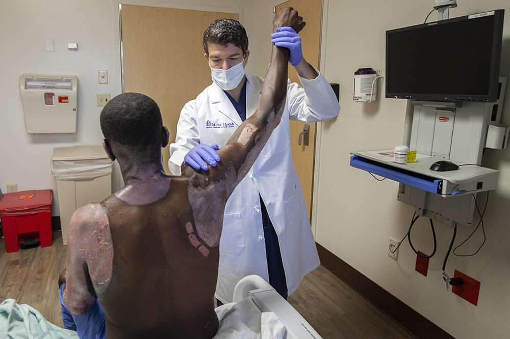 Dr. Stephen Kahn raises the right arm of Tommy Porcha to examine Porcha's burns.