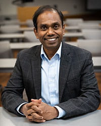 a man sits at a desk in a classroom and smiles at the camera