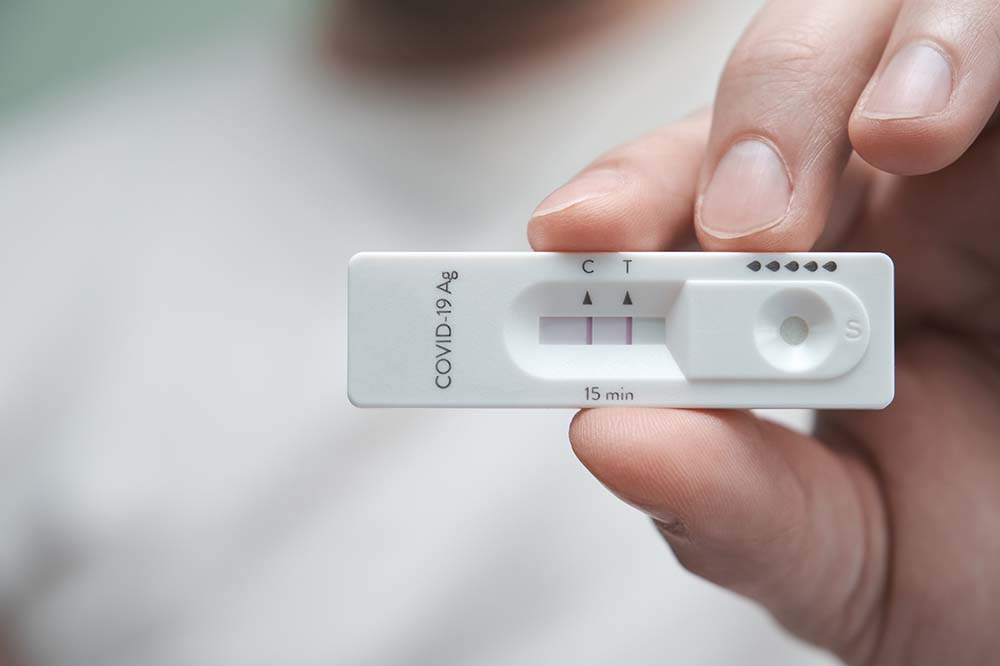 Closeup of a hand holding a home COVID test. It shows a positive result.