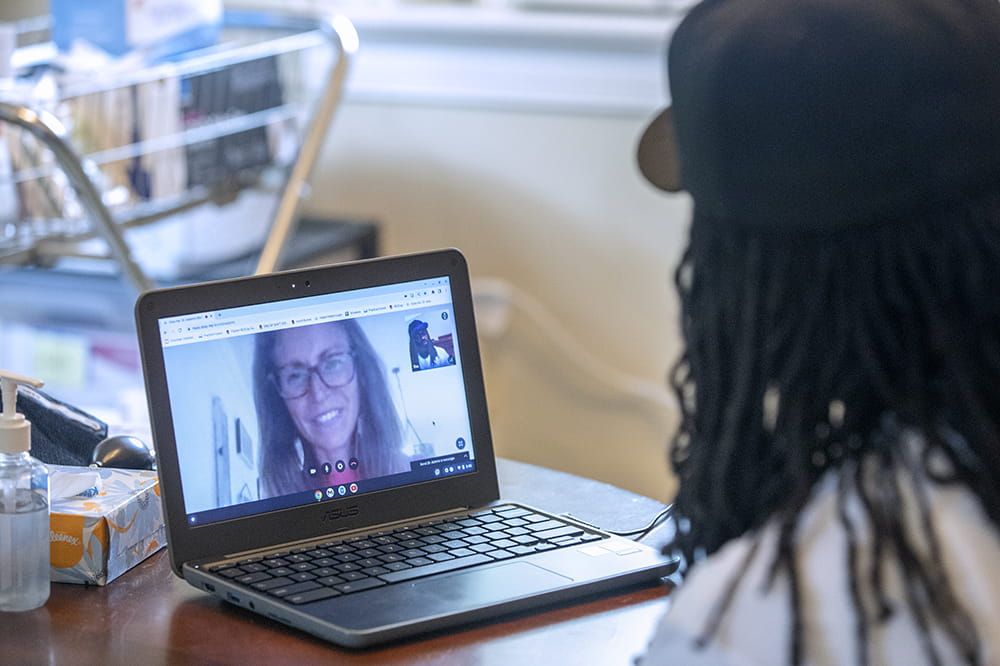 A doctor, whose face can be seen on a laptop, remotely interacts with a patient