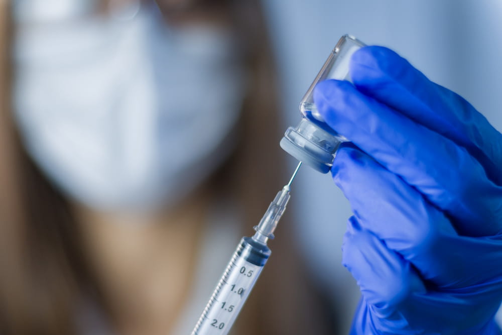 close up of syringe being stuck into vial of vaccine