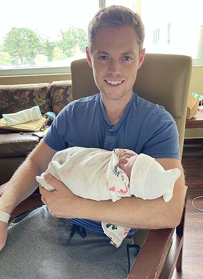 Cory and Liam Robertson. Cory is sitting in a chair holding his newborn son.