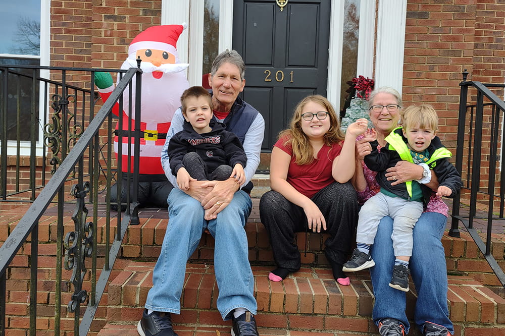 a man and woman sit on the brick front steps of a house with a girl between them and a boy in each lap and an inflatable Santa Claus behind them