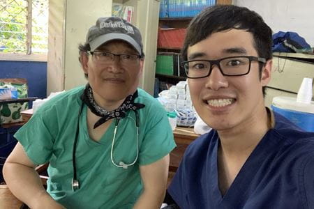 two men wearing scrubs, one the father, the other the son, smiling for a selfie