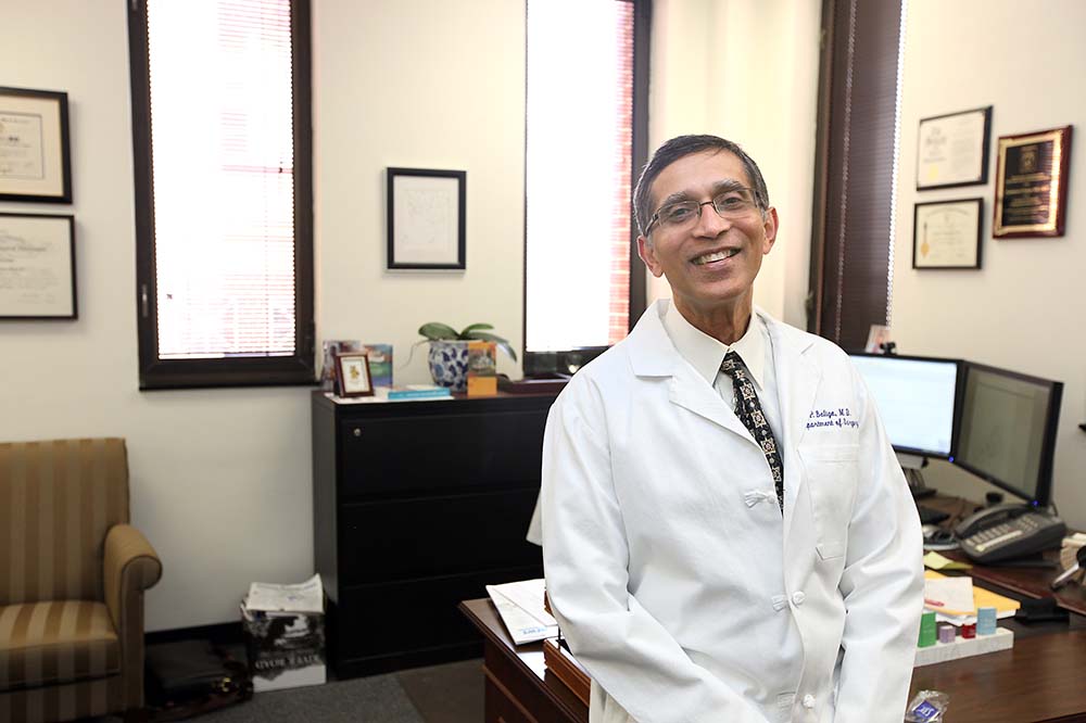 Dr. Prabhakar Baliga in an office. The chairman of the Department of Surgery is wearing a white doctor's coat and smiling.