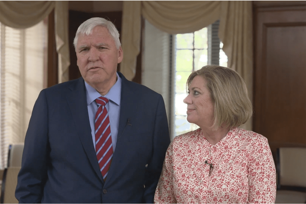MUSC President David Cole is wearing a navy suit coat and a tie. He's speaking while his wife, Kathy, listens. She is wearing a pink top. The photo is from a video for the 2022 Service Awards.