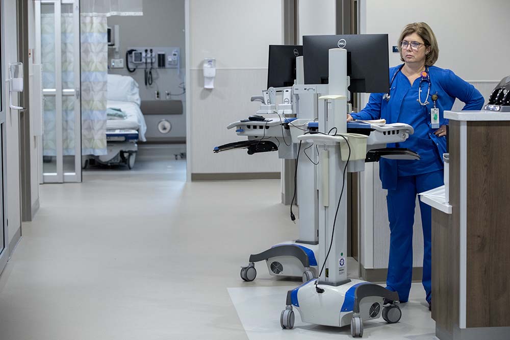Woman in blue scrubs works at a computer monitor.