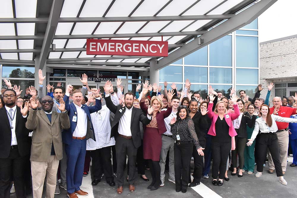 People standing outside hospital raise hands while posing fora large group photo.