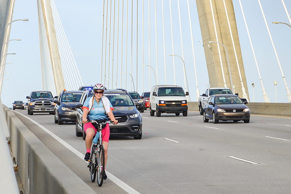 a sole bicyclist in the narrow shoulder of the bridge followed by cars