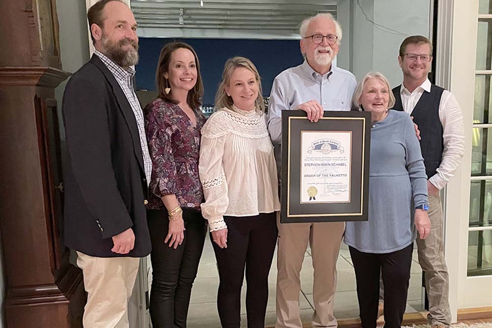 A bearded man holds a plaque. He's surrounded by three women and two other men. They are all smiling.