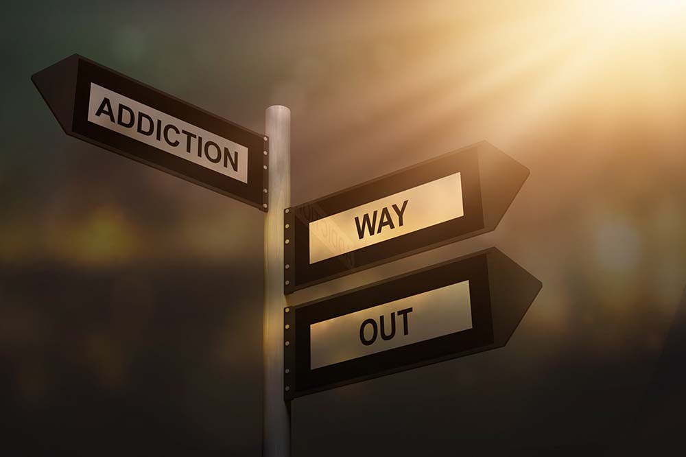 Signpost with the word addiction on the left side and the words way out on the other side.