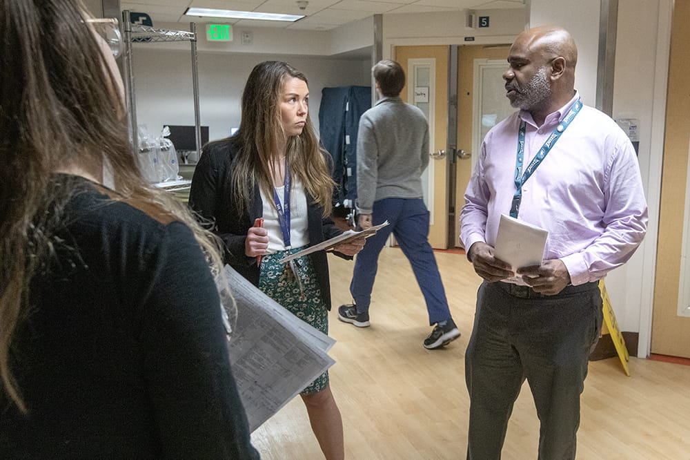 Woman with long hair holding a clipboard talks intently to a man wearing a dress shirt. He looks serious as well.