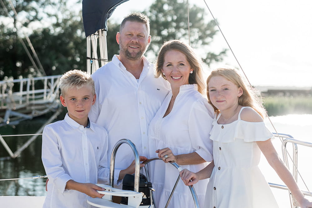 a mom, dad, boy and girl, all dressed in white, pose on a sailboat