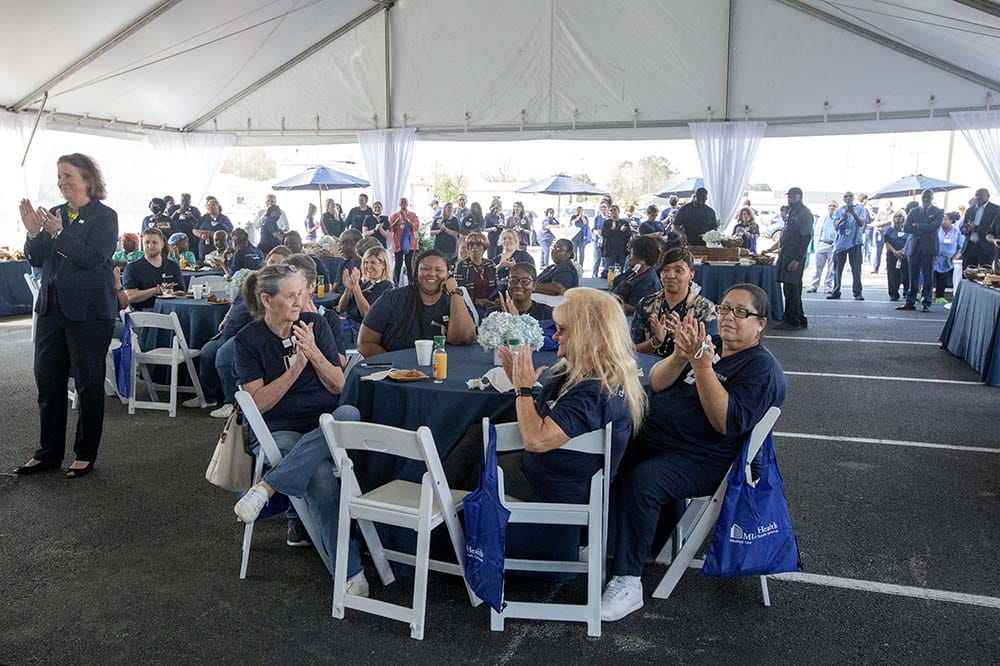 A group of women wearing navy uniforms sits in white chairs at a table eating and talking.