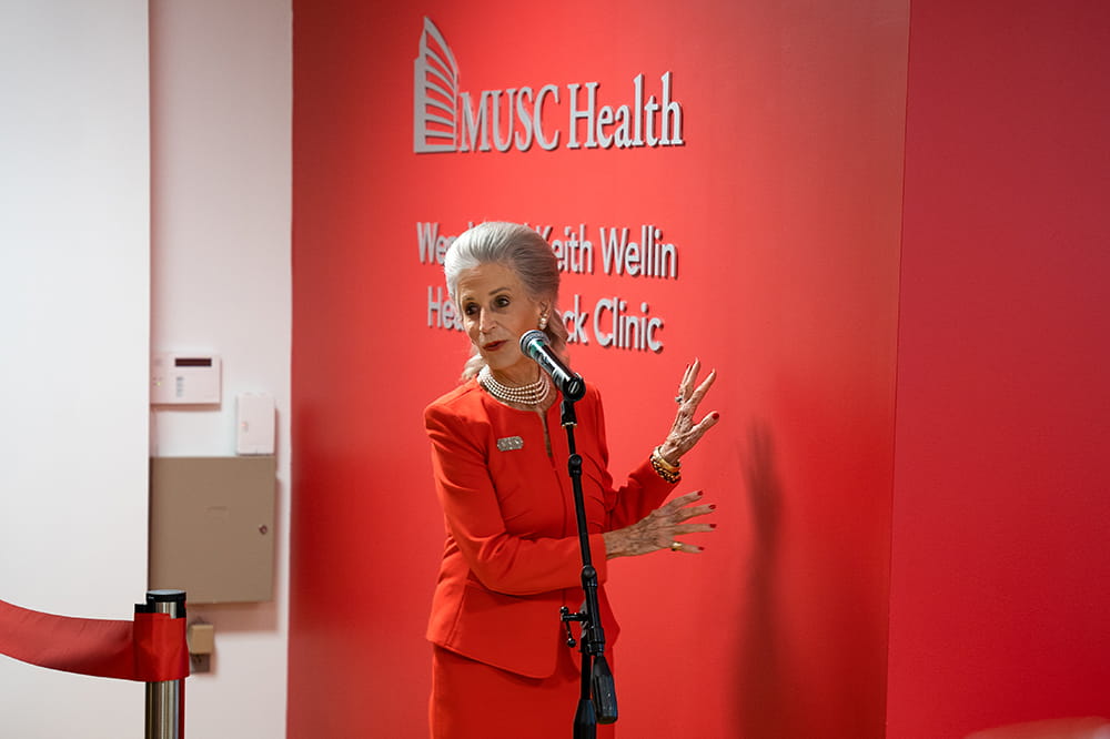 a woman in a red suit gestures toward a red wall behind her