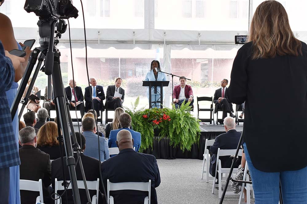 Woman wearing a blue suit speaks at a podium. A large audience sits before her.