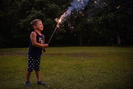 a young boy with a sparkler, standing in grass