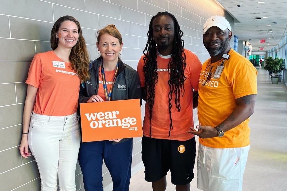 Four people, all wearing orange, stand in a hallway smiling