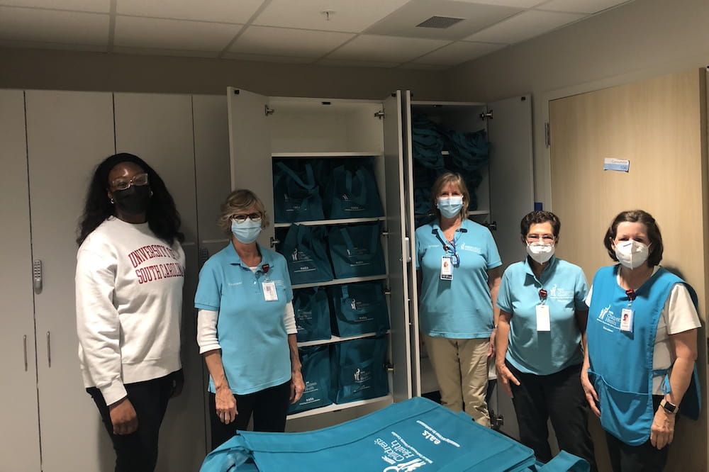 Five volunteers in blue shirts stand in front of a pantry filled with bags of food