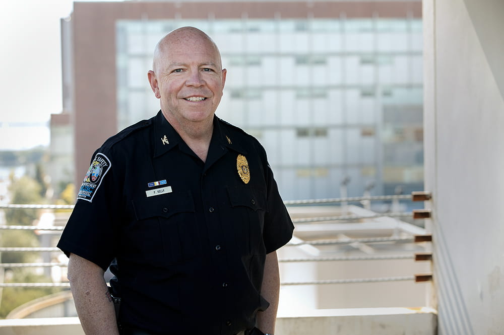 Man in a blue police uniform smiles. There is a large building behind him.