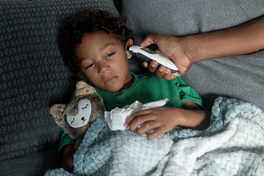 Little boy holding stuffed animal gets his temperature checked.