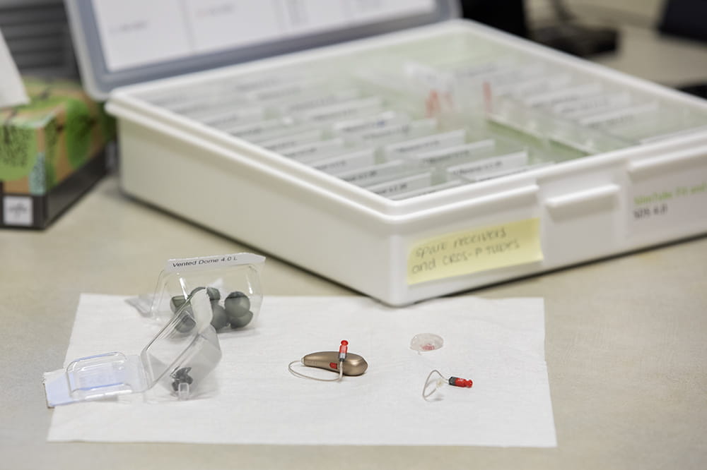 Small hearing aids and parts sit on a white napkin in front of an open box.