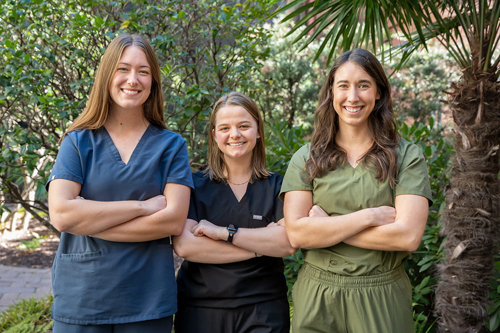 three young women occupational therapy students in scrubs pose together in the garden
