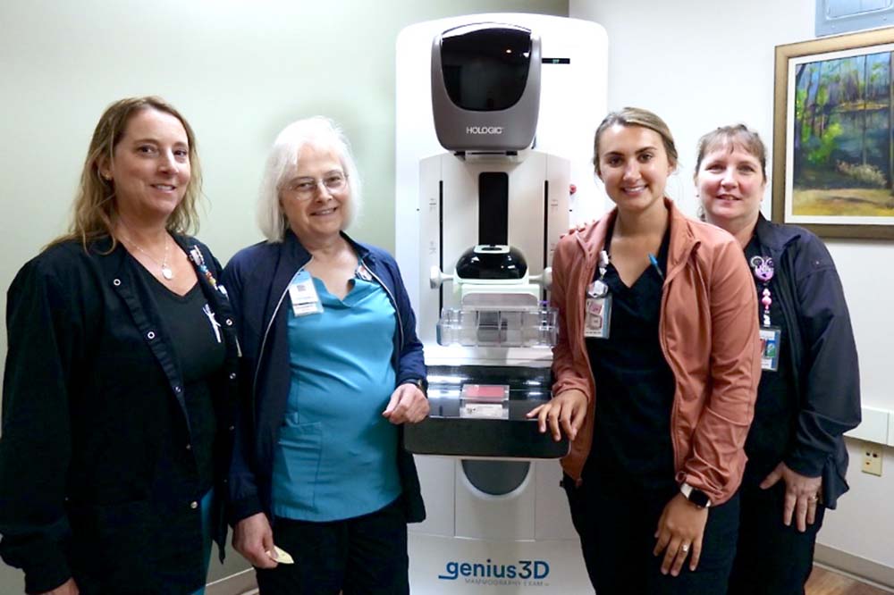 Four women stand around a 3D mammogram machine.