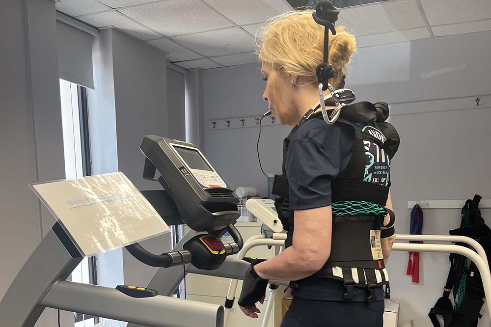 Woman in black exercise clothes walks on a treadmill wearing medical monitoring devices.