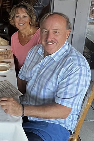 a couple in business casual look up from a white tablecloth table and smile at the camera