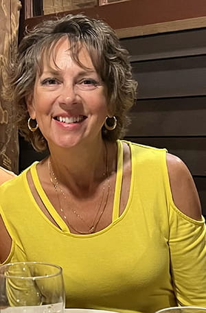 a woman in a yellow cold-shoulder top sitting at a restaurant smiles at the camera