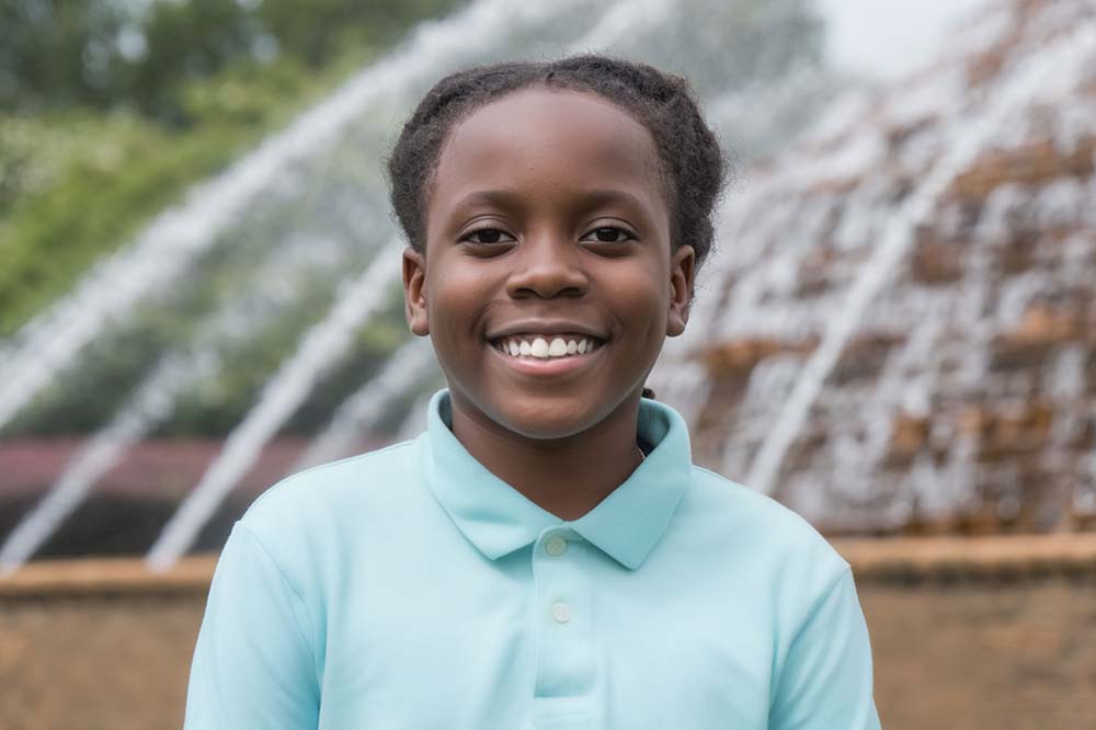 Young man stands in front of a water fountain. He is smiling. 