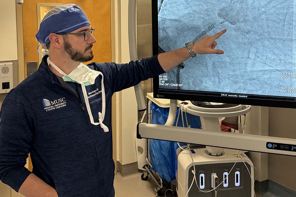 Man in hospital scrubs points to a screen.