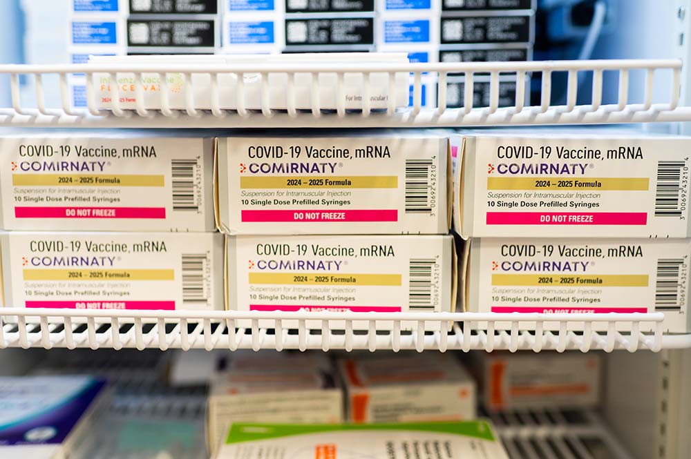 Six boxes of COVID vaccines on a white shelf.