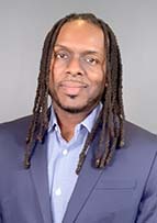 Headshot of a man with long braided hair. He is wearing a dress shirt and suit jacket.