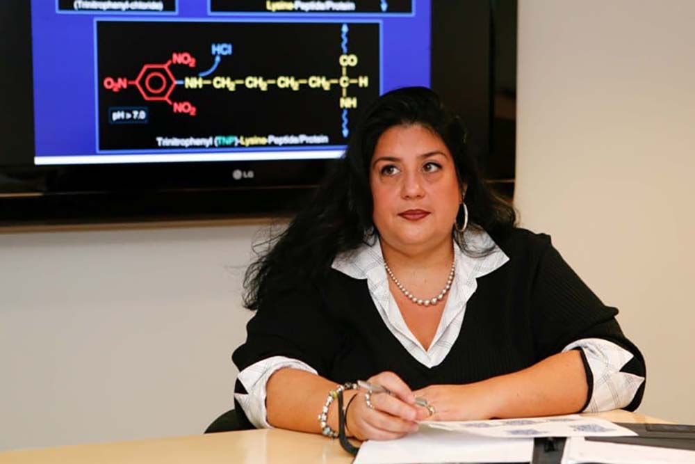 A woman with long dark hair sits at a table taking notes.