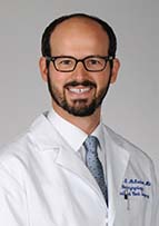 Smiling man with a beard and eyeglasses wearing a white doctor's coat.