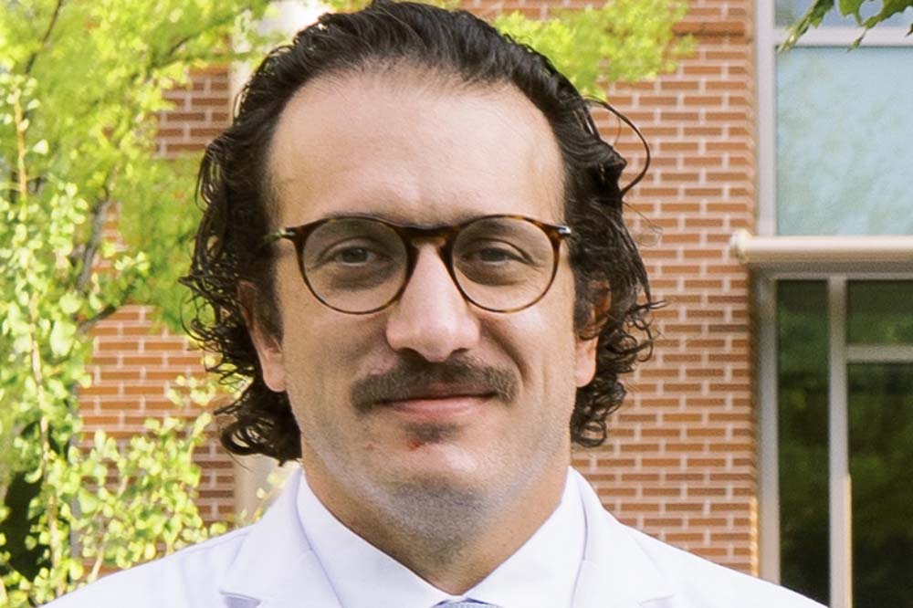 Headshot of a man with dark hair and a mustache. He's wearing glasses and a white doctor's coat.