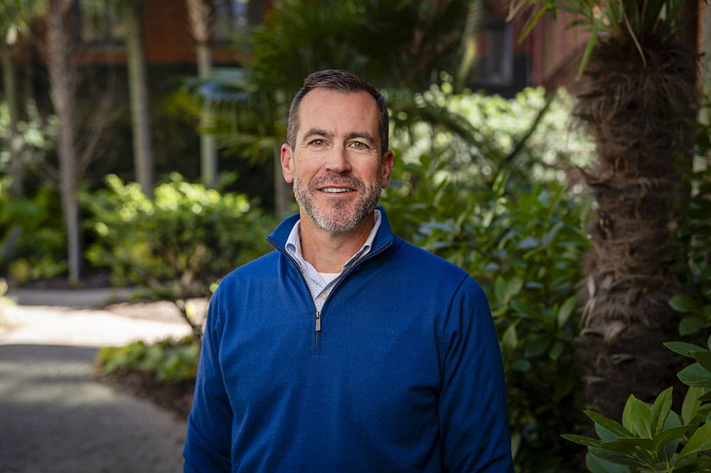 a man in a blue pullover to represent colon cancer poses in a garden setting