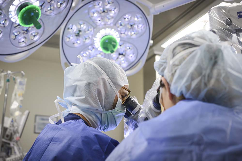 In an operating room, doctors in scrubs wearing head coverings look down at a patient.