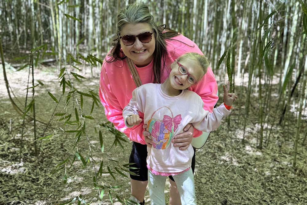 A woman wearing a pink top and sunglasses with a girl in a brightly colored outfit.