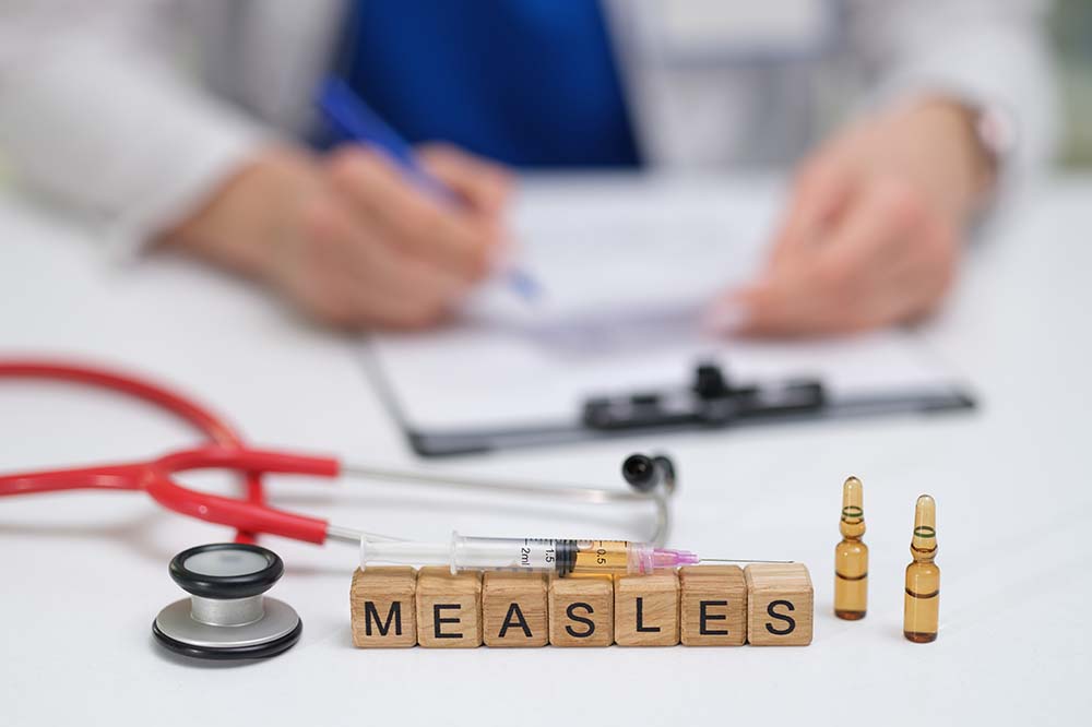 Blocks spell the word "measles." there is a stethoscope beside them and a woman's hands working on a clipboard.