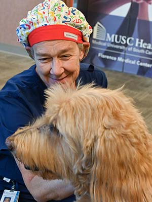 A woman wearing a cap and scrubs with a strawberry blonde dog, who is facing to the left side.