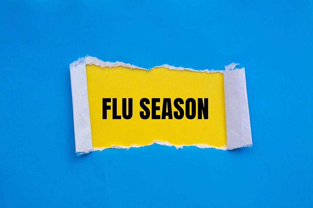 The words flu season are written in black on yellow. Blue paper overlays it and is being peeled back to show the words.