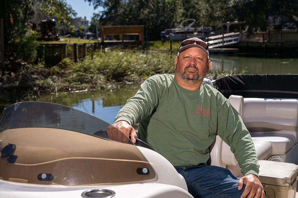 a man poses in the captain's chair of his pontoon boat
