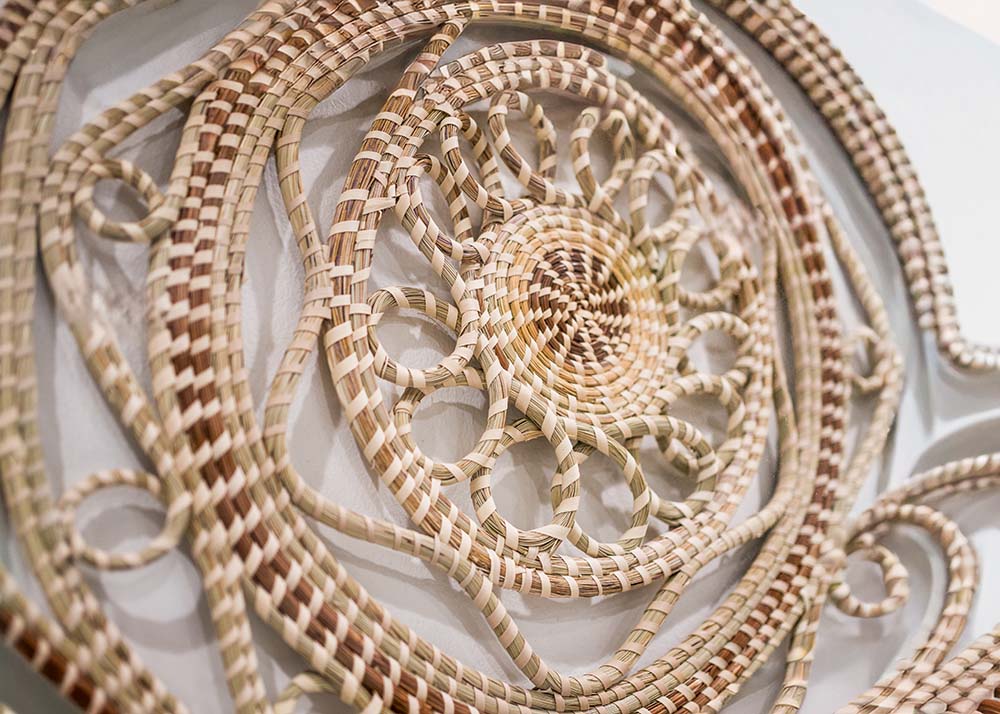 A beautiful work of sweetgrass hanging on a wall. It has a spiral motif.